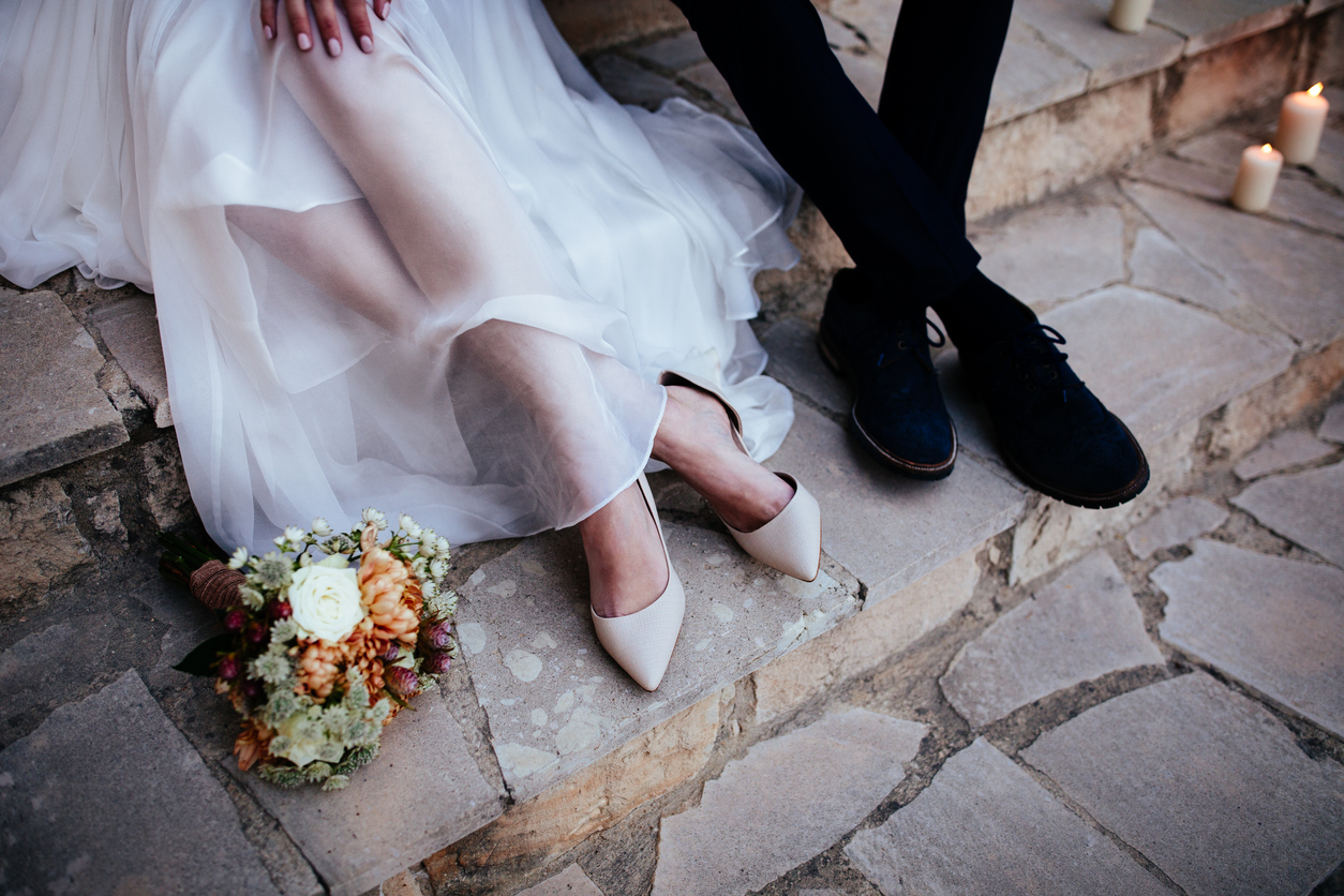 Close-up of bride and groom with flower bouquet sitting together on stone staircase outdoors